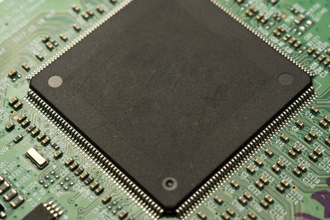 Primer plano detallado de un componente Ball Grid Array (BGA) de paso fino montado en una placa de circuito impreso de control industrial compleja y de alta densidad durante el proceso de ensamblaje del BGA.